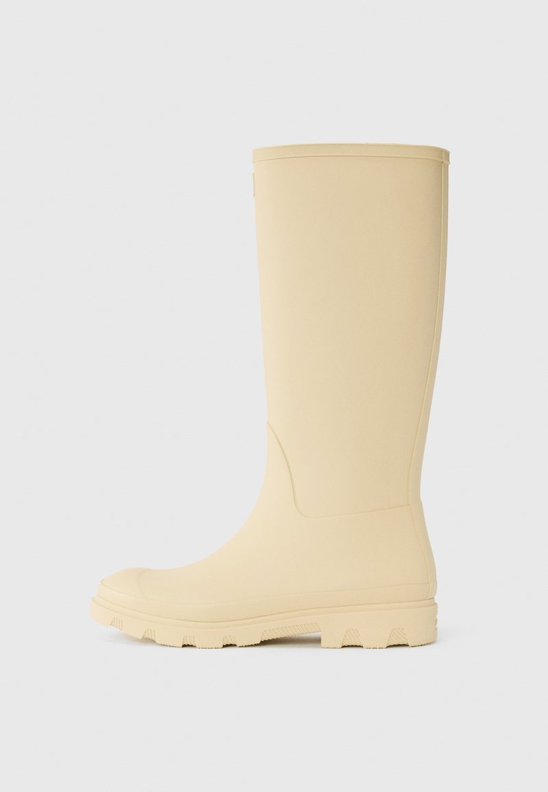 Beige rubber rain boot with a flat sole, rounded toe, and textured footbed. Smooth surface and a slightly raised edge at the top.