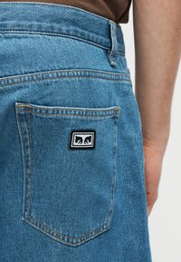 Πίσω τσέπη μπλε τζιν με ένα μικρό ασπρόμαυρο φιλέτο που δείχνει δύο στυλιζαρισμένες σιλουέτες αρκούδων που κοιτάζονται η μία την άλλη.