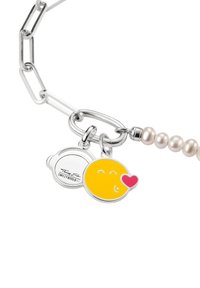 Silberarmband mit Kette, das einen gelben Smiley-Anhänger mit einem roten Herz sowie einen runden Anhänger mit Markenlogo zeigt, ergänzt durch weiße Perlen.