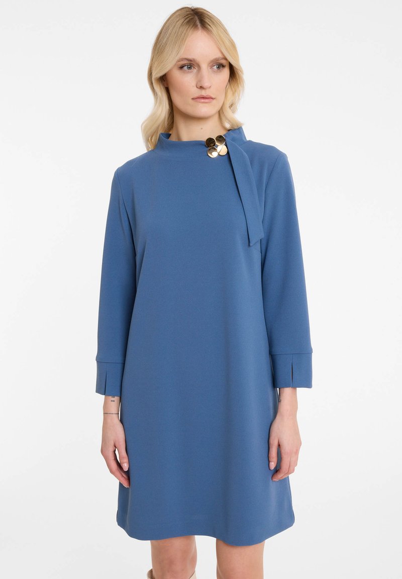Robe bleue midi en tissu doux, avec un col haut, des manches longues et des boutons en accent doré au niveau du col.