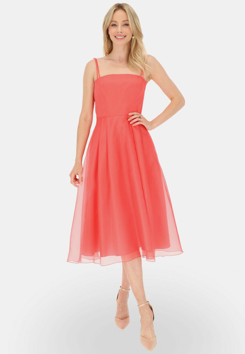 Koralowa sukienka midi na cienkich ramiączkach, dopasowany biust, oraz zwiewna, warstwowa spódnica. Teksturowany materiał, przezroczysta nakładka i sandały na kostkę.