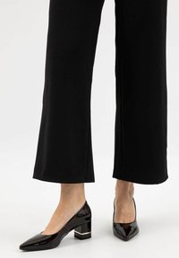 Décolleté in vernice nera con punta affusolata, tacco a blocco e un accento dorato alla base. Indossati con pantaloni neri a gamba larga.