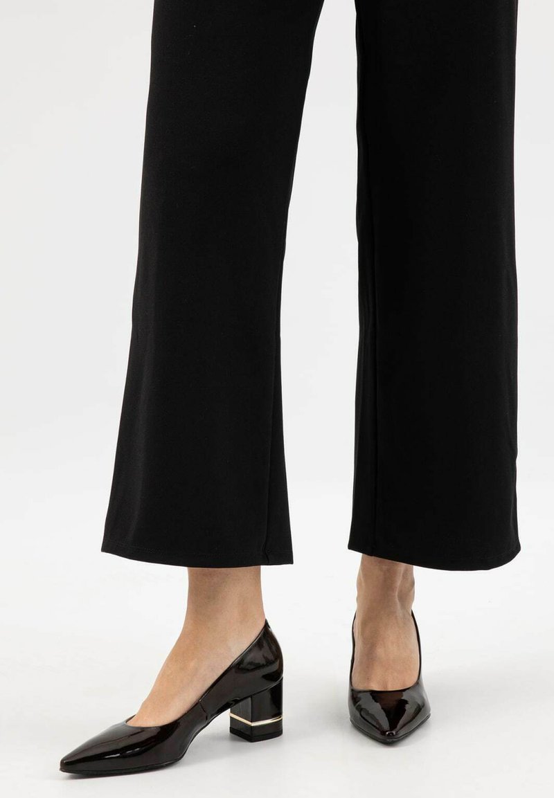 Décolleté in vernice nera con punta affusolata, tacco a blocco e un accento dorato alla base. Indossati con pantaloni neri a gamba larga.