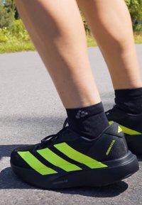 Schwarze Laufschuhe mit fluoreszierenden gelben Streifen und Akzenten, hergestellt aus atmungsaktivem Material, mit einer strukturierten Sohle für besseren Halt.