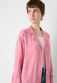 Light pink button-up shirt with a subtle textured pattern, featuring a classic collar and long sleeves, paired with a white undershirt.
