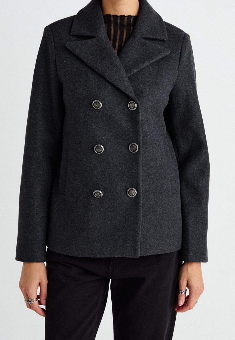 Blazer de lana gris de doble botonadura con grandes botones, solapa muesca y bolsillos laterales. Presenta un ajuste entallado y una textura suave.