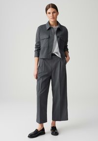 Grijze cropped jas met twee voorzakken, gecombineerd met grijze wijde pantalons met fijne streep en zwarte loafers. Getextureerde stof en rechte snit.