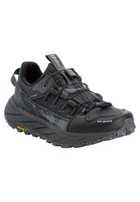 Scarpa da trail running nera con tomaia testurizzata, lacci elastici e colletto imbottito. Caratterizzata da una suola Vibram con dettagli maculati.