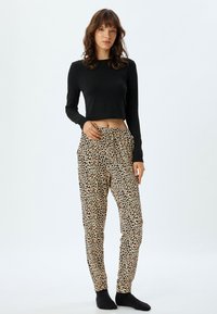 Zwarte cropped lange mouwen top met een ronde halslijn, gecombineerd met beige leopardprint comfortabele broek met een trekkoord, zijzakken en taps toelopende pijpen.