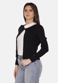 Cardigan nero con scollatura arrotondata, maniche lunghe e un taglio leggermente accorciato. Realizzato in un tessuto knit leggero, presenta un logo discreto.