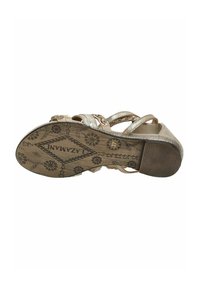 Beige Sandalen verfügen über geflochtene Riemen mit metallischen Akzenten, eine strukturierte Innensohle und eine gemusterte Sohle mit floralen Motiven.