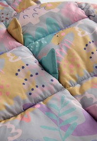 Tissu matelassé coloré avec des formes de dinosaures ludiques et des pointes en tissu cousues en jaune et bleu sarcelle le long des coutures.