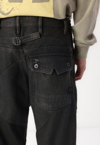 Sorte denim cargo bukser med flere lommer, en teksturert finish, og et unikt design på baklommen. Justerbar midje inkludert.