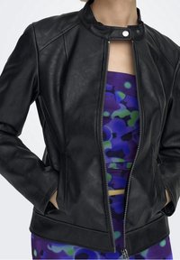 Giubbino in pelle nera con colletto alto, chiusura con zip, tasche laterali e un design leggermente aderente. Indossato sopra un top viola a fantasia.