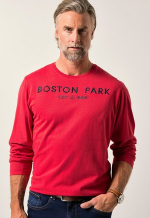 Rød langærmet T-shirt lavet af bomuld, med "BOSTON PARK EST 1996" trykt i mørkeblå over brystet, og rund halsudskæring.