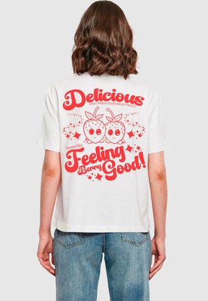 Weißes Baumwoll-T-Shirt mit oversized Passform, ausgestattet mit rotem Text und verspielten Erdbeer-Grafiken auf der Rückseite. Kurzärmelig und mit Rundhalsausschnitt.