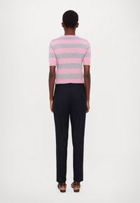 Maglione corto a maniche corte con righe orizzontali rosa e grigie, con scollatura tonda. Abbinato a pantaloni scuri e sandali.