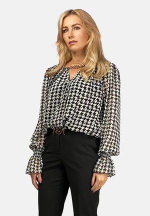 Czarna i biała bluzka w wzór houndstooth z przezroczystymi rękawami i falbaniastymi mankietami, w zestawie z czarnymi spodniami i metalicznym paskiem.