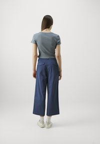 Modrá halenka s krátkým rukávem v kombinaci s volnými námořnickými culottes. Kalhoty mají zadní kapsy a hladkou texturu. Bílé boty a ponožky do půli lýtek.