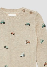 Beige gestrickter Pullover mit kleinen gestickten Traktoren in Grün und Braun. Rundhalsausschnitt mit zwei braunen Druckknöpfen an der Schulter zur Befestigung.