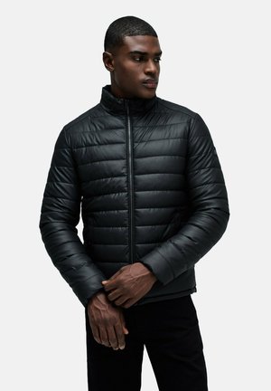 Chaqueta de plumas negra con cuello alto, diseño acolchado, cremallera frontal y bolsillos laterales. Textura suave y silueta ajustada.