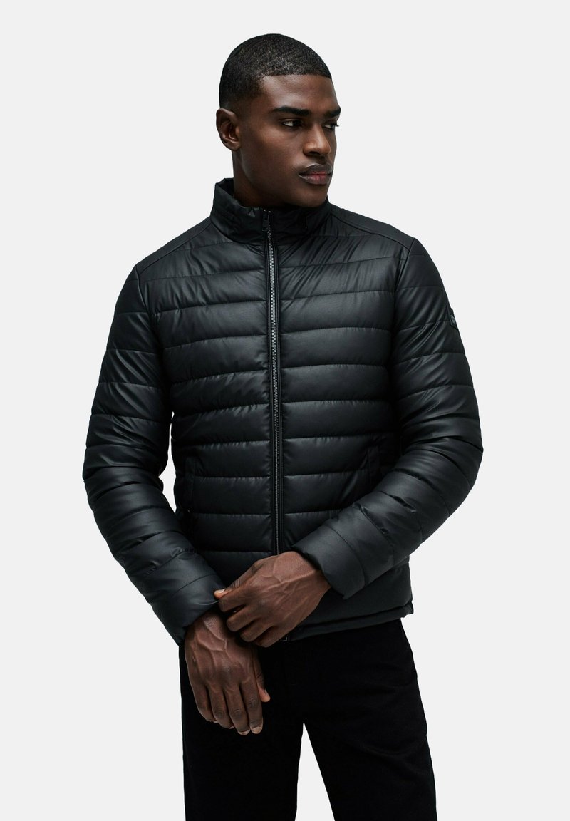 Giacca a vento nera con collo alto, design trapuntato, zip frontale e tasche laterali. Texture liscia e silhouette aderente.