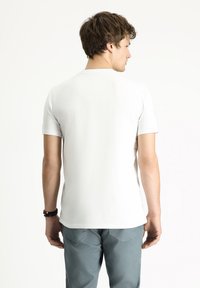 Camiseta blanca de manga corta hecha de algodón, con un diseño liso y un dobladillo recto. La parte trasera es sencilla y no tiene gráficos ni logotipos visibles.