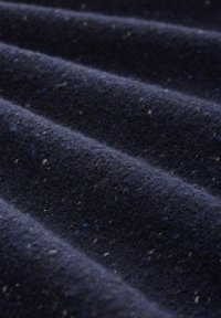 Närbild av mörkblå ulltyg med en mjuk, fnasig textur och subtila inslag av ljusblå och vita fibrer.