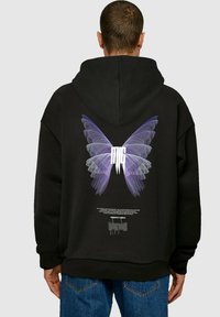 Felpa nera con cappuccio caratterizzata da un grande grafico di farfalla viola sul retro, con dettagli leggeri e testo sottostante. Tessuto morbido, vestibilità ampia.