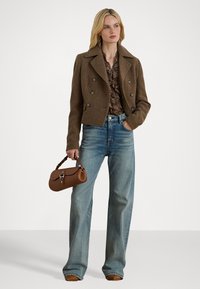Brun dobbeltspent jakke, mønstret bluse, lyseblå vide jeans og en liten brun håndveske med kort stropp.