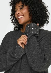 Tamno sivi pulover s rebrastim manžetama sa srebrnim zakovicama; mekana tekstura i opušteni kroj, ističući jedinstvenu detalj rukava.