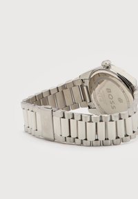 Ρολόι χειρός από ανοξείδωτο ατσάλι με μπρασελέ από μεταλλικούς κρίκους, κούμπωμα αναδιπλούμενο με εγχάραξη "BOSS" και πίσω μέρος κάσας με την επωνυμία, που δείχνει λεπτομέρειες αντοχής στο νερό.