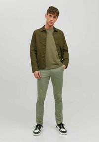 Veste en coton vert olive, t-shirt assorti et pantalon slim-fit vert clair. Baskets noires et blanches avec lacets. Design simple et polyvalent.