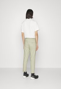 Abgeschnittenes weißes T-Shirt kombiniert mit hellgrünen Hosen, die einen Kordelzugbund haben. Von hinten sind schwarze Schuhe mit strukturierten Sohlen sichtbar.