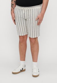 Shorts rayés crème avec des lignes navy, dotés d'une taille à cordon de serrage ajustable. Associés à des baskets blanches et des chaussettes côtelées.