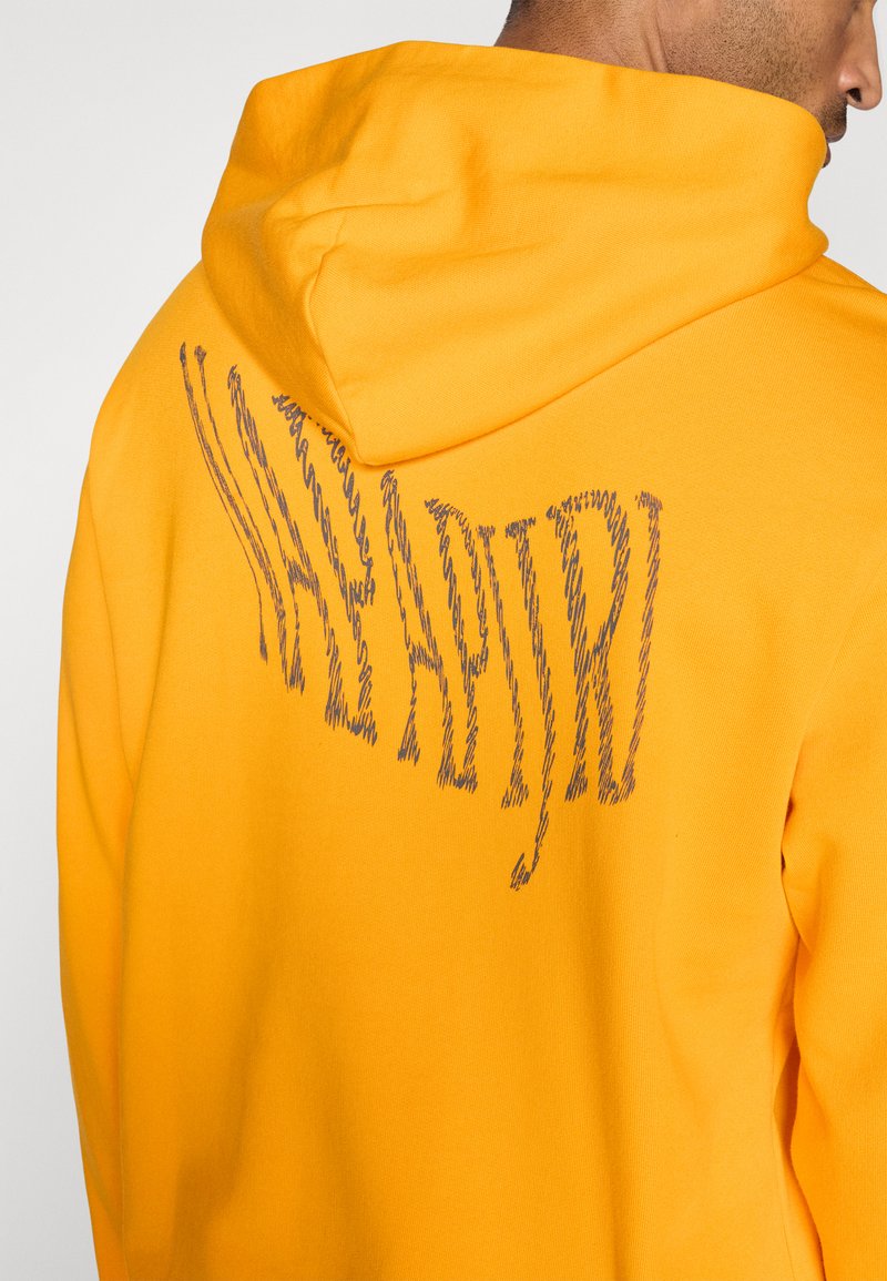 Gelber Hoodie mit einer strukturierten, kontrastierenden Grafik in Grau auf dem Rücken, mit einer Kordelzugkapuze und einem weichen Stoffgefühl.