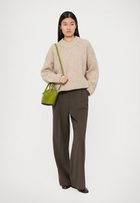 Beżowy sweter z dzianiny w serek, w połączeniu z brązowymi spodniami o szerokich nogawkach. Mała zielona torebka o sztywnym fasonie.