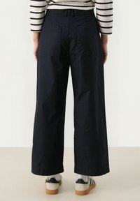 Wide-leg navy pants made of cotton, featuring two back pockets and a high waist. Styled with a striped top and casual sneakers.