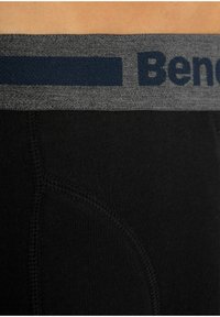 Schwarze Boxershorts mit einem grauen elastischen Bund, der ein dunkelblaues Logo trägt. Der Stoff wirkt glatt und hat ein enganliegendes Design mit abgesetzten Nähten.