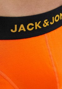 Orange Stretchbaumwoll-Boxerbriefs mit einem schwarzen elastischen Bund, der gelben "JACK & JONES"-Schriftzug trägt. Nahtdetails sind auf dem Stoff sichtbar.
