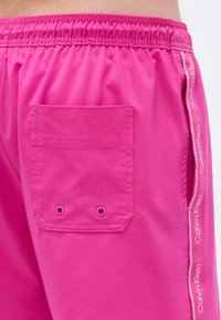 Ροζ σορτς με ελαστική  μέση, πίσω τσέπη με μεταλλικές τρύπες και πλαϊνές ραφές διακοσμημένες με την επωνυμία "Calvin Klein".