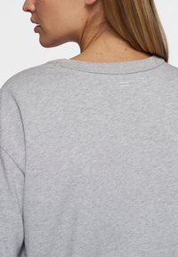 Sudadera gris con cuello redondo, hombros caídos y un pequeño detalle de costura horizontal en la parte trasera. Tejido suave y texturizado.