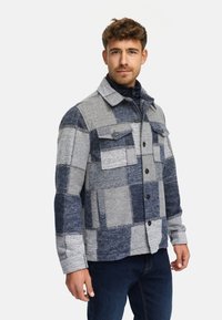 Marineblå og grå rutete flanelljakke med to brystlommer, knappelukking og nedbrettbar krage. Myk tekstur og varmt design.