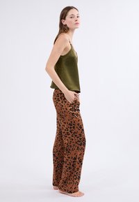 Camiseta de satén verde oliva con tirantes finos, combinada con pantalones anchos marrones con un patrón de leopardo negro.