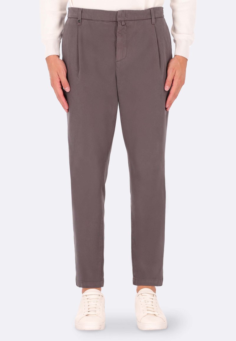 Pantaloni grigi a pieghe con una trama liscia, vestibilità affusolata, tasche laterali e passanti per cintura, abbinati a sneakers bianche.