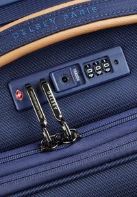 Valigia blu navy in tessuto testurizzato, dotata di lucchetto a combinazione TSA, cerniere in metallo e un accento in pelle sintetica.