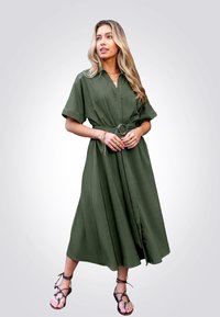 Vestido verde hasta la rodilla, hecho de una tela ligera, con mangas cortas y un cinturón. Presenta un escote en V y una silueta fluida.