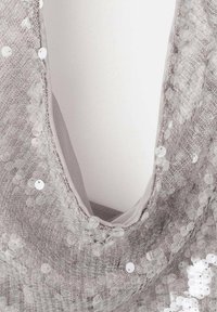 Srebrna sukienka z cekinami bez rękawów z głębokim dekoltem w kształcie V oraz przezroczystym materiałem pod spodem, prezentująca skomplikowane teksturowane detale.