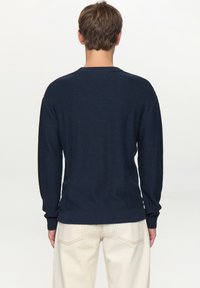 Donkerblauwe gebreide trui met lange mouwen, ronde hals en geribbelde zoom. Zachte textuur, getailleerd model, gezien van achteren.