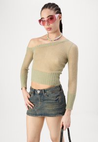 Pletena, off-shoulder džemper u svijetlozelenoj boji s rebrastim rubom; uparena s plavim traper mini suknjom. Nositi ružičaste prozirne sunčane naočale i ogrlicu od perlica.